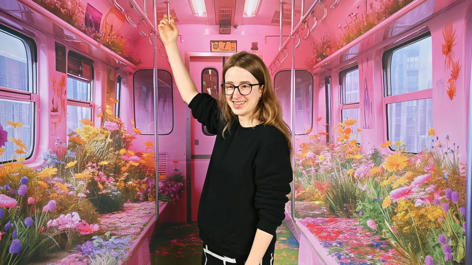 Luna Spiegel lacht mit erhobenem Arm, umgeben von einer knallbunten, blumenförmigen Kunstinstallation.
