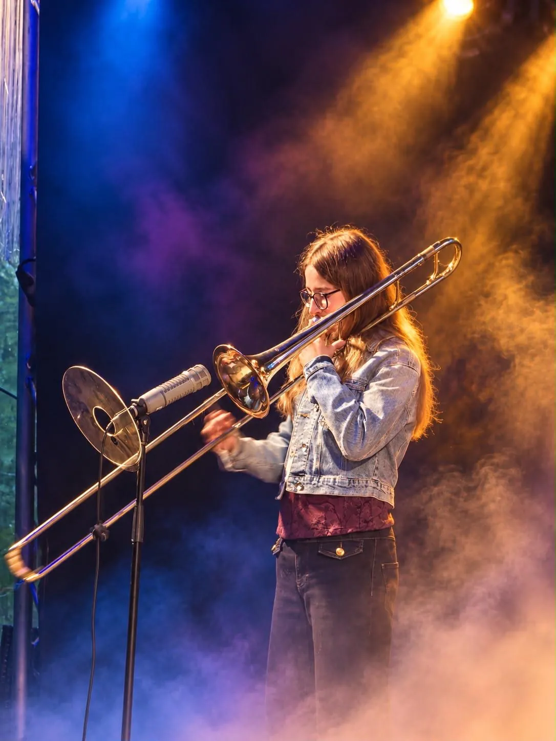 Luna Spiegel spielt Posaune auf der Bühne, angestrahlt von blauem und goldenem Scheinwerferlicht im Bühnennebel.